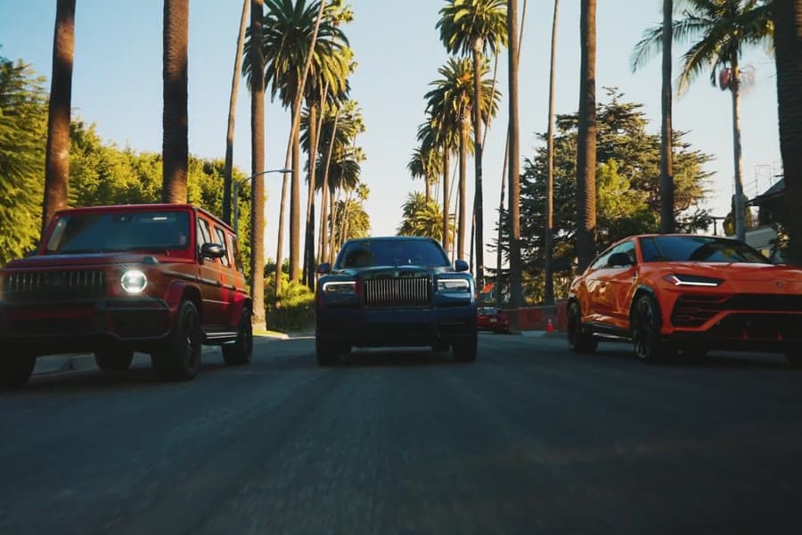 Three luxury SUVs on a palm-lined street